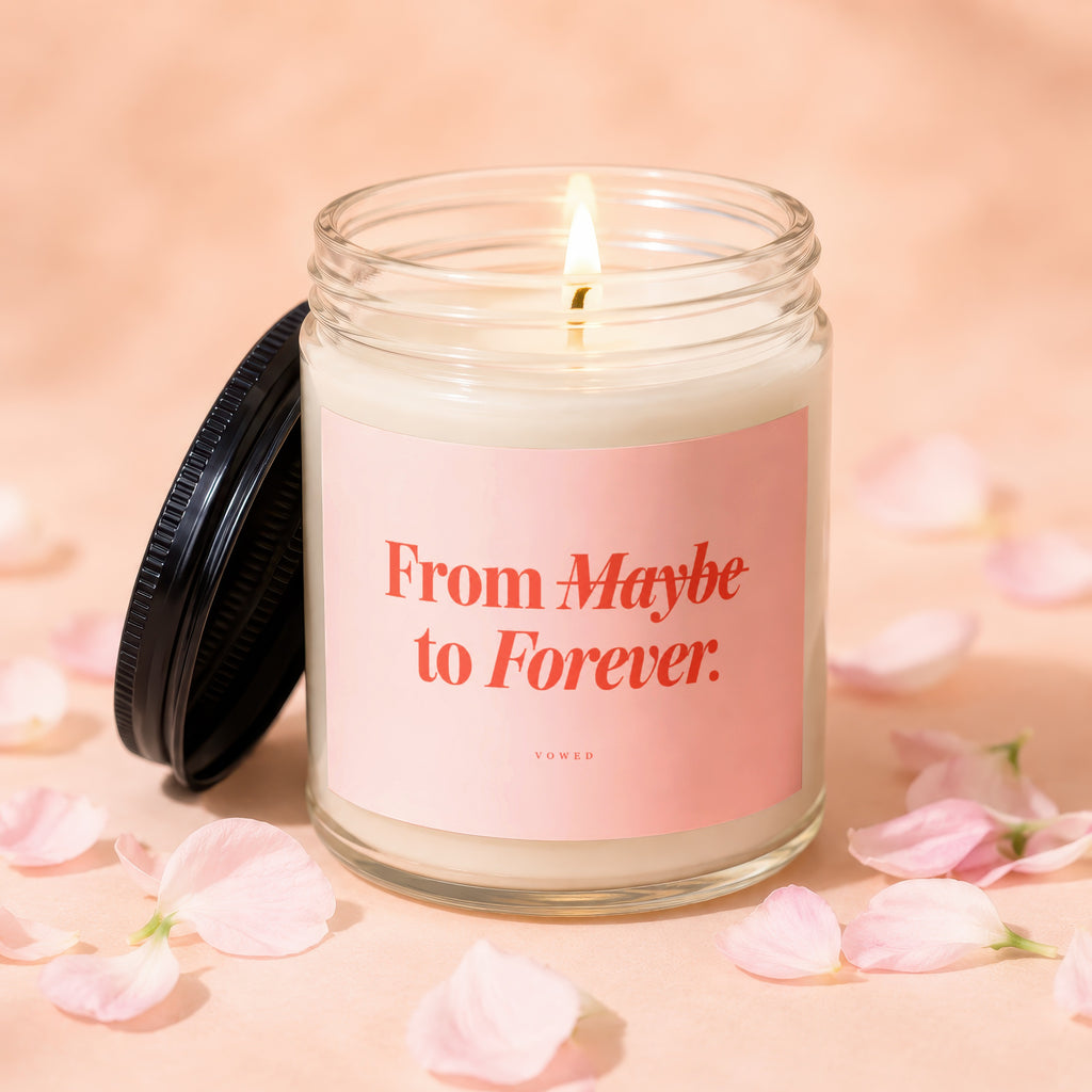 Lit candle in glass jar with pink label reading "From Maybe to Forever. VOWED".