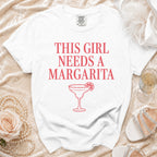 White t-shirt with "This girl needs a Margarita" text and margarita graphic.