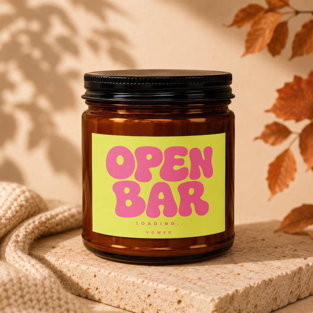 Amber jar candle with bright yellow label reading "OPEN BAR LOADING... VOWED".