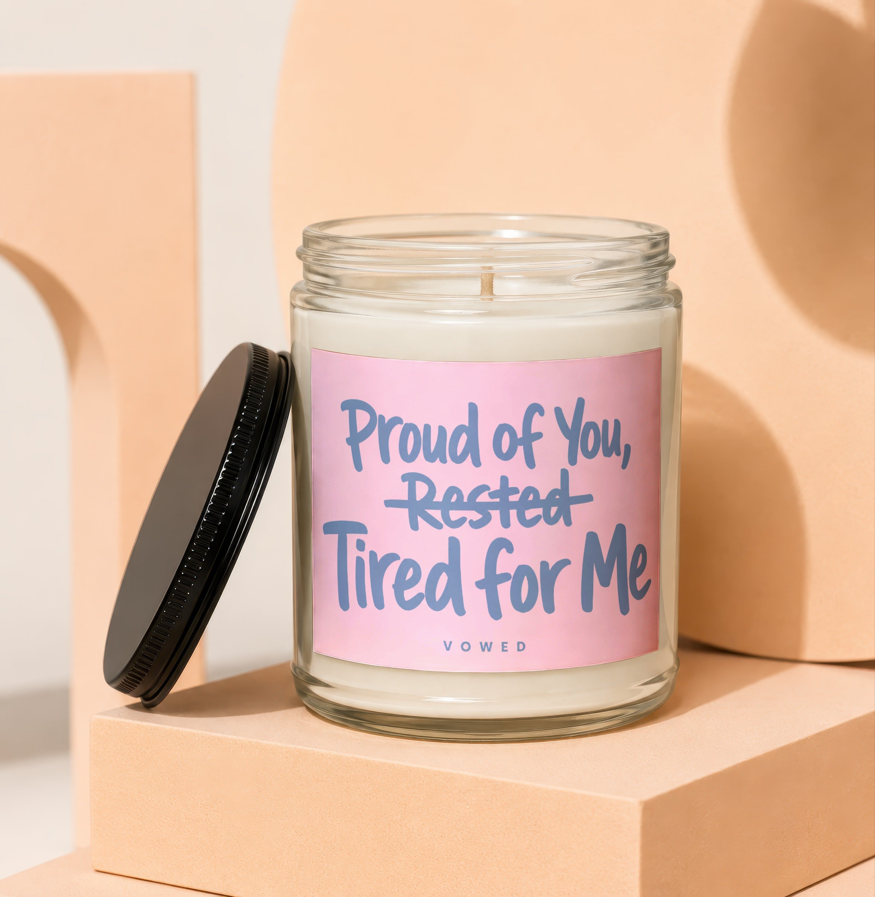 Glass candle with pink label reading "Proud of You, Rested Tired for Me".
