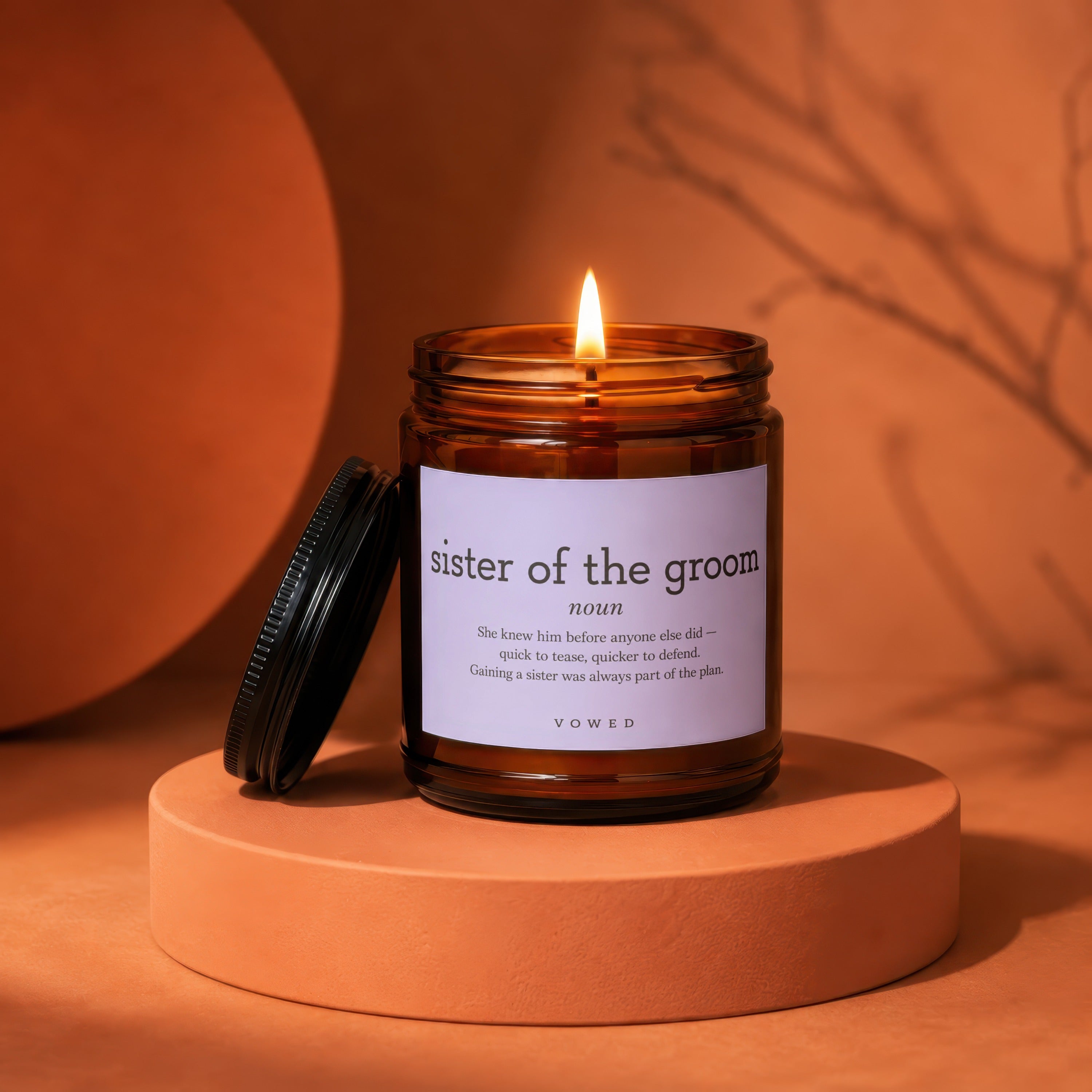 Amber jar candle with lit flame, labeled "sister of the groom," on an orange circular stand.