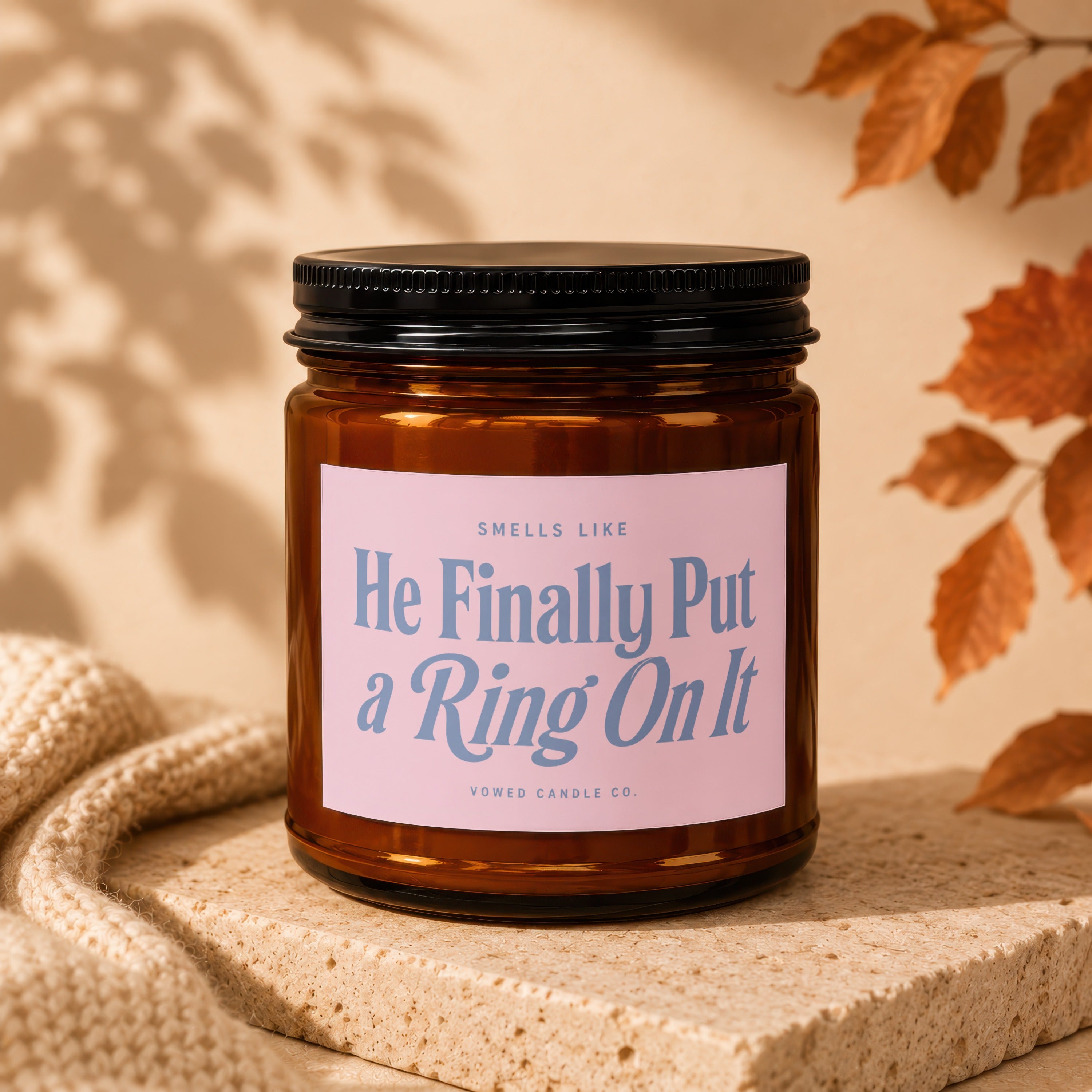 Amber jar candle with pink label reading "He Finally Put a Ring On It"