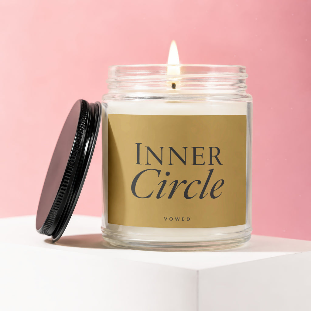 Candle with "Inner Circle" and "vowed" text on gold label, lid removed, lit flame.