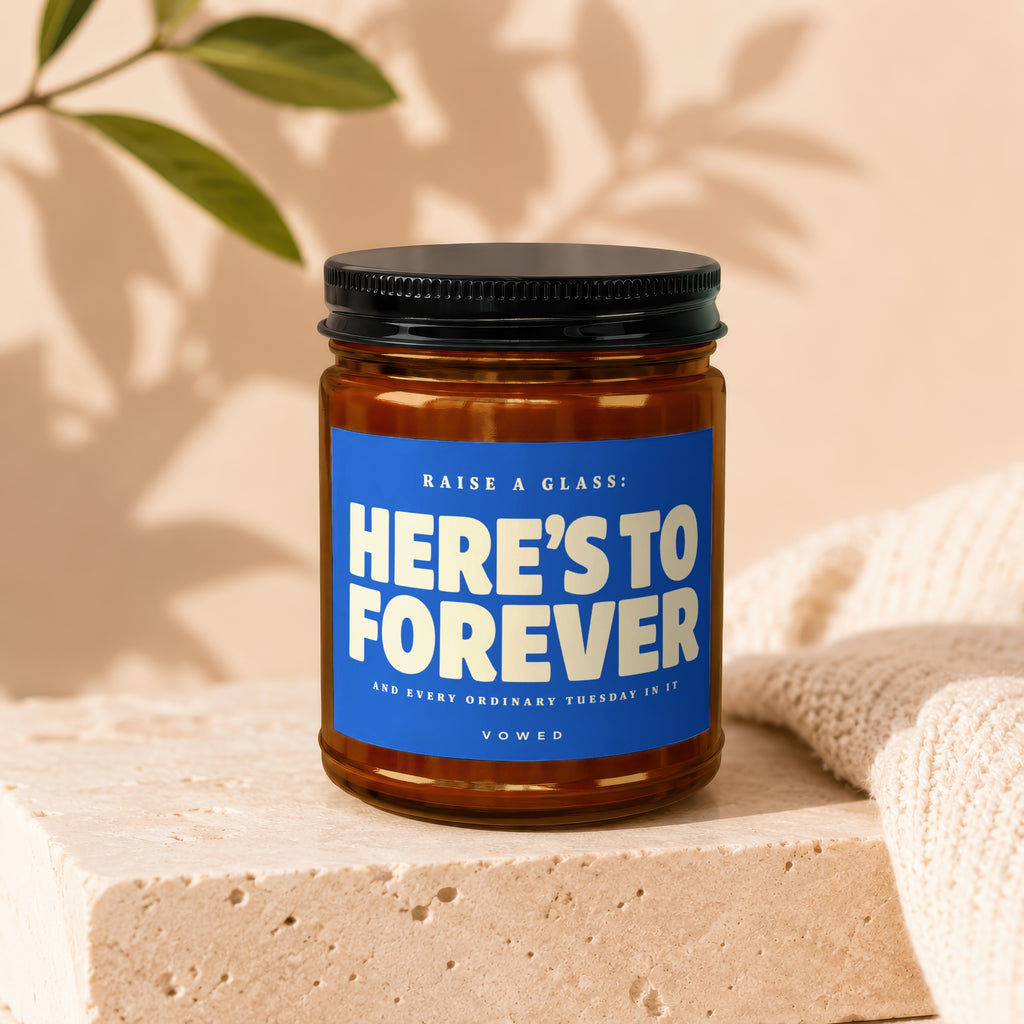 Brown glass jar with black lid, blue label reads "RAISE A GLASS: HERE'S TO FOREVER AND EVERY ORDINARY TUESDAY IN IT VOWED".