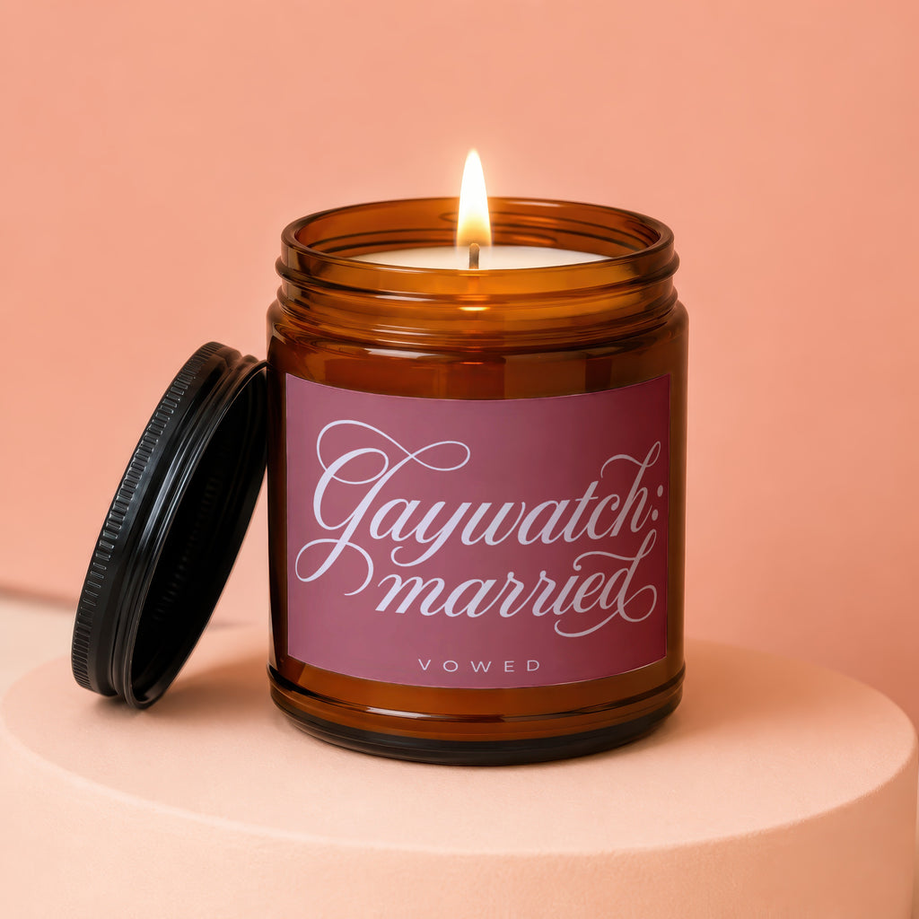 Amber jar candle with lit wick and label reading "Gaywatch: married VOWED".