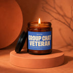 Candle with lit wick and label reading "GROUP CHAT VETERAN" on a display stand.