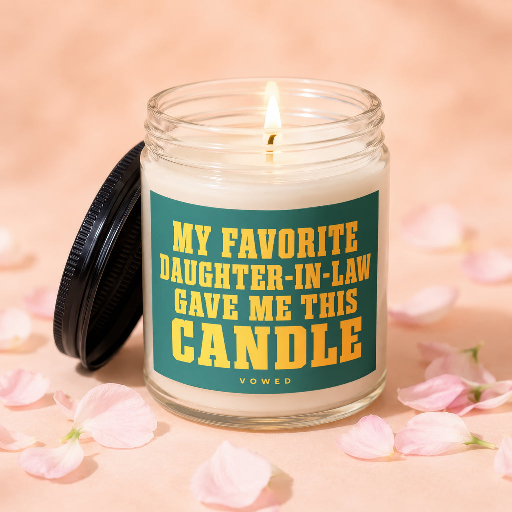 Jar candle with a lit wick and a black lid, displaying the text "MY FAVORITE DAUGHTER-IN-LAW GAVE ME THIS CANDLE".