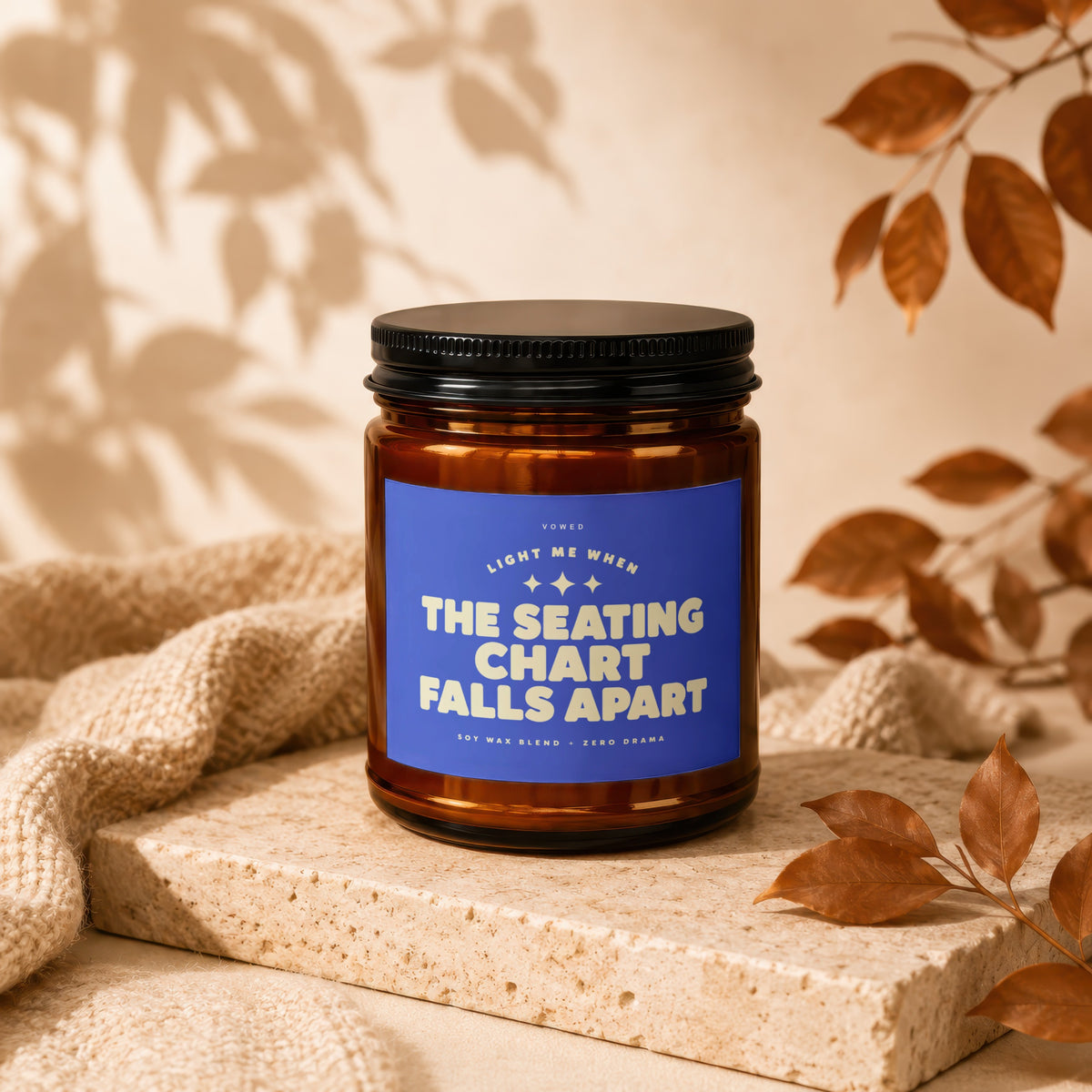 Amber jar candle with blue label reading "Light Me When The Seating Chart Falls Apart."
