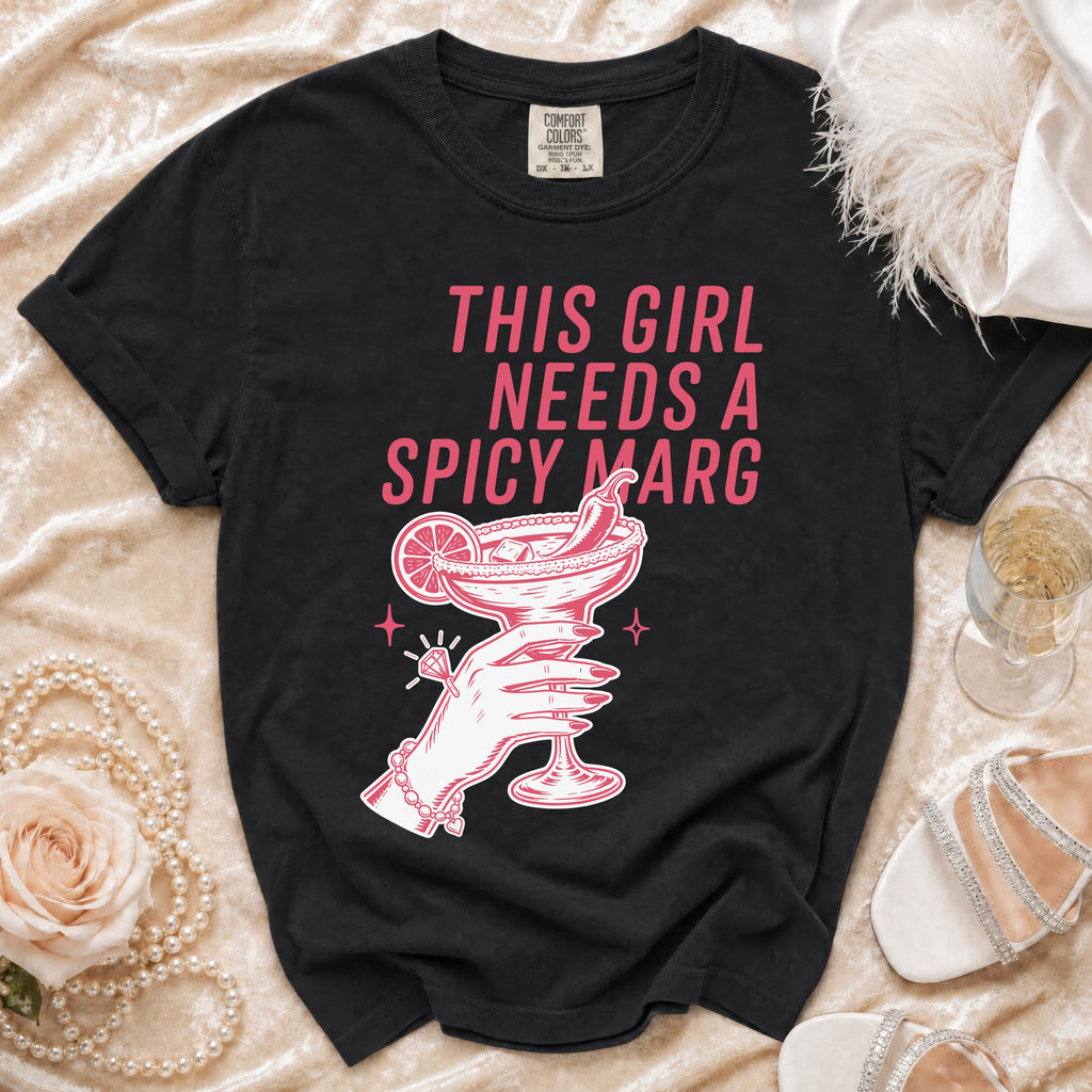 Black t-shirt with pink graphic of hand holding spicy margarita, "THIS GIRL NEEDS A SPICY MARG".