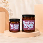 Two amber glass candles with "Two grooms, no notes, no chill" text, set on pedestals.