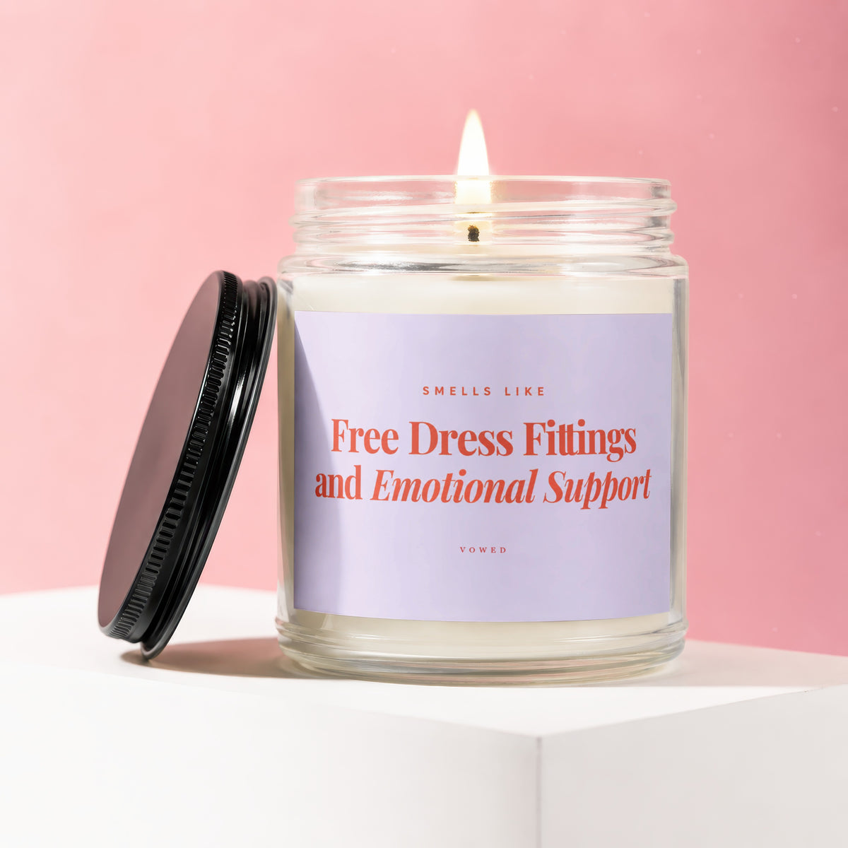 Lit candle in jar with lid off, reading "Smells Like Free Dress Fittings and Emotional Support".