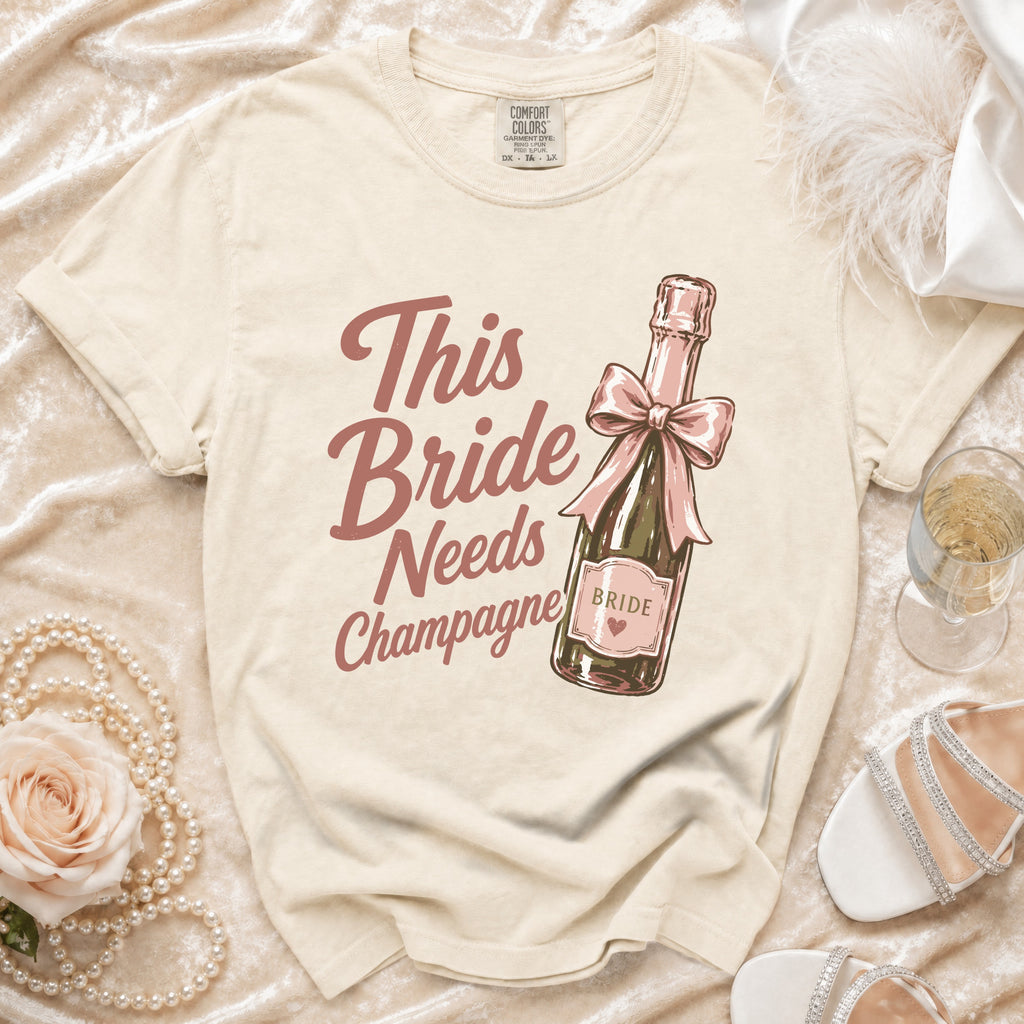 T-shirt with vintage style graphic of champagne bottle. Text reads "This Bride Needs Champagne".