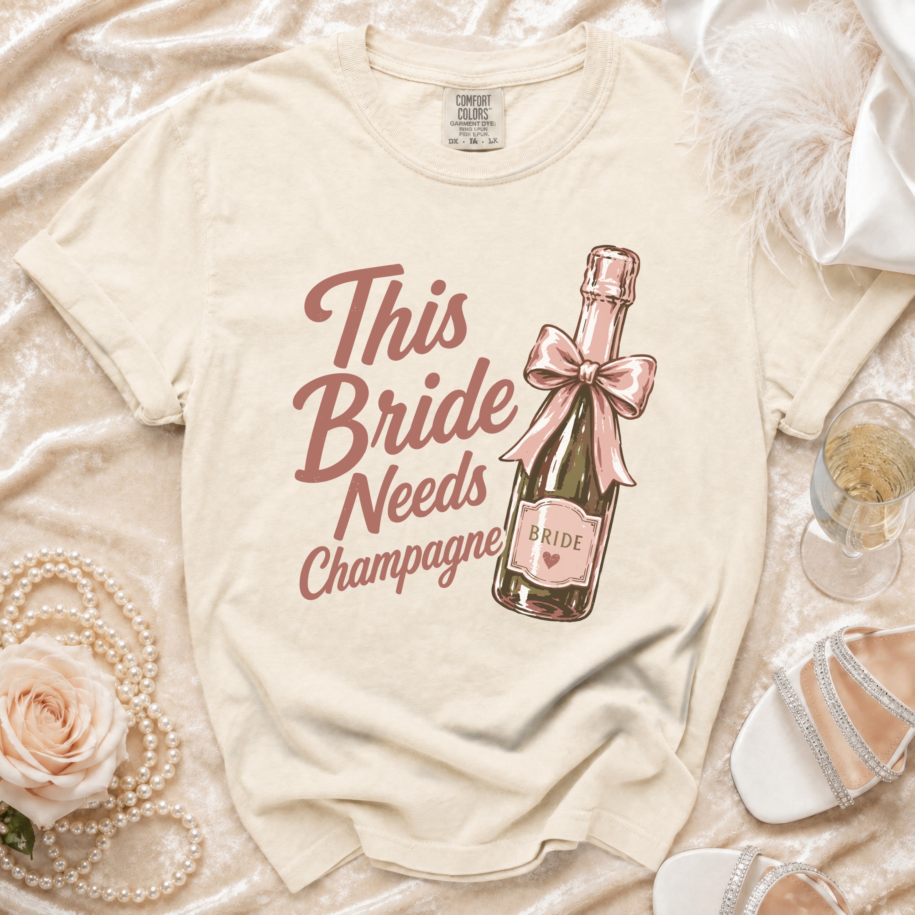 T-shirt with vintage style graphic of champagne bottle. Text reads "This Bride Needs Champagne".