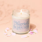 Lit candle in a jar with label "Married the plot twist VOWED" surrounded by petals.