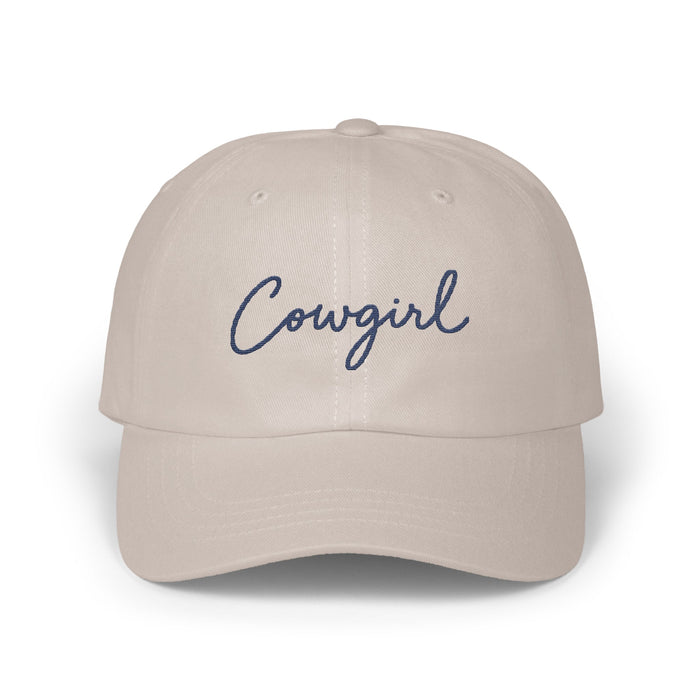 Light beige baseball cap with the word Cowgirl embroidered in navy blue cursive script.