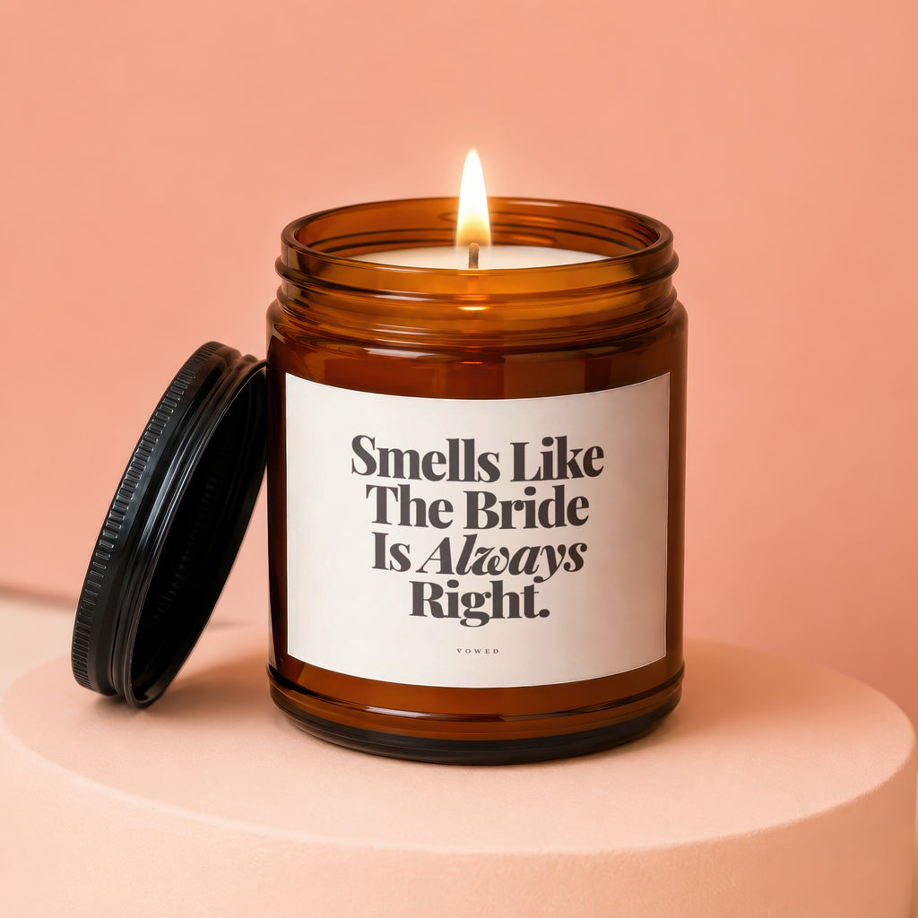 Amber glass candle with lit wick, black lid off to the side, and text "Smells Like The Bride Is Always Right."