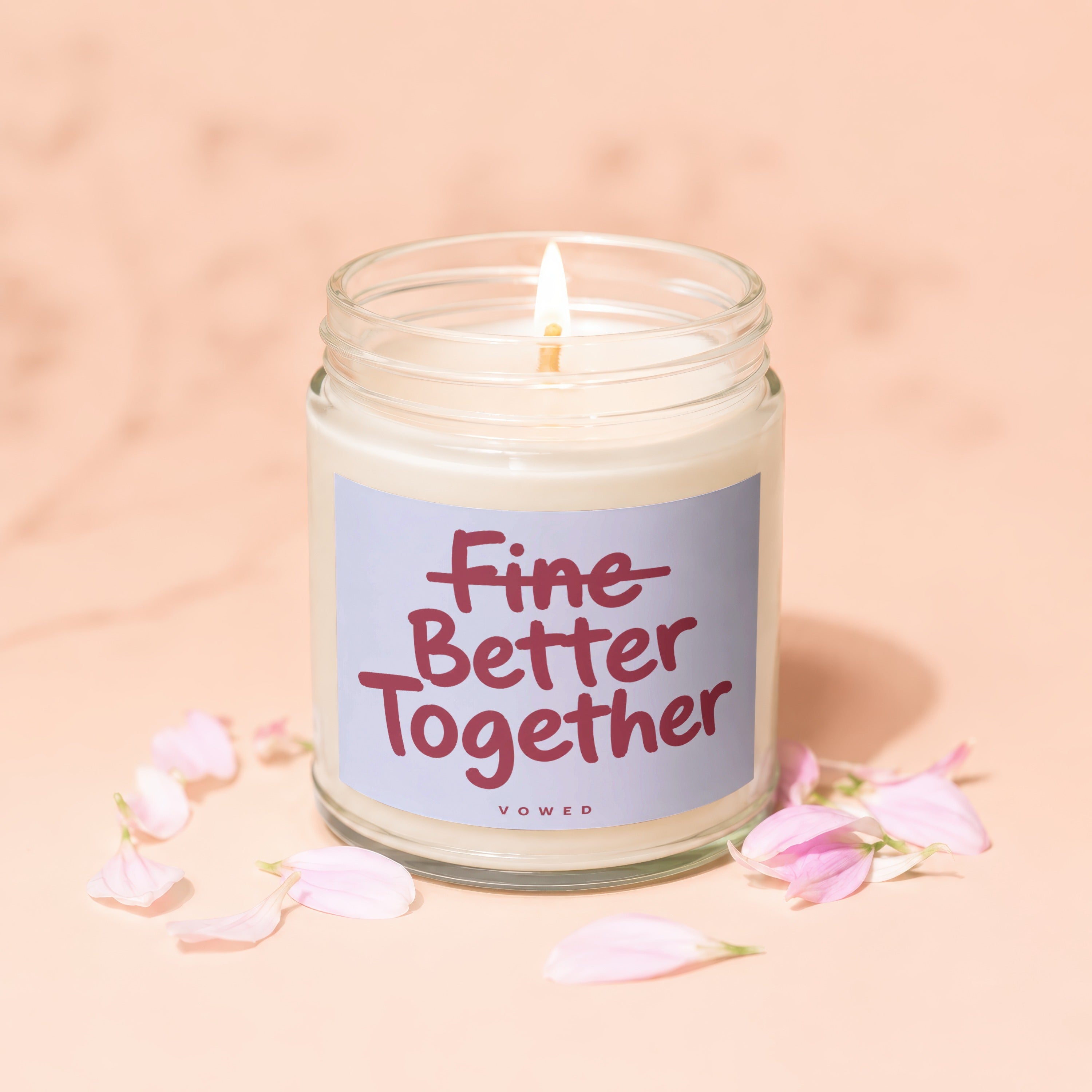 Candle with "Fine Better Together" text on label amidst peach petals.