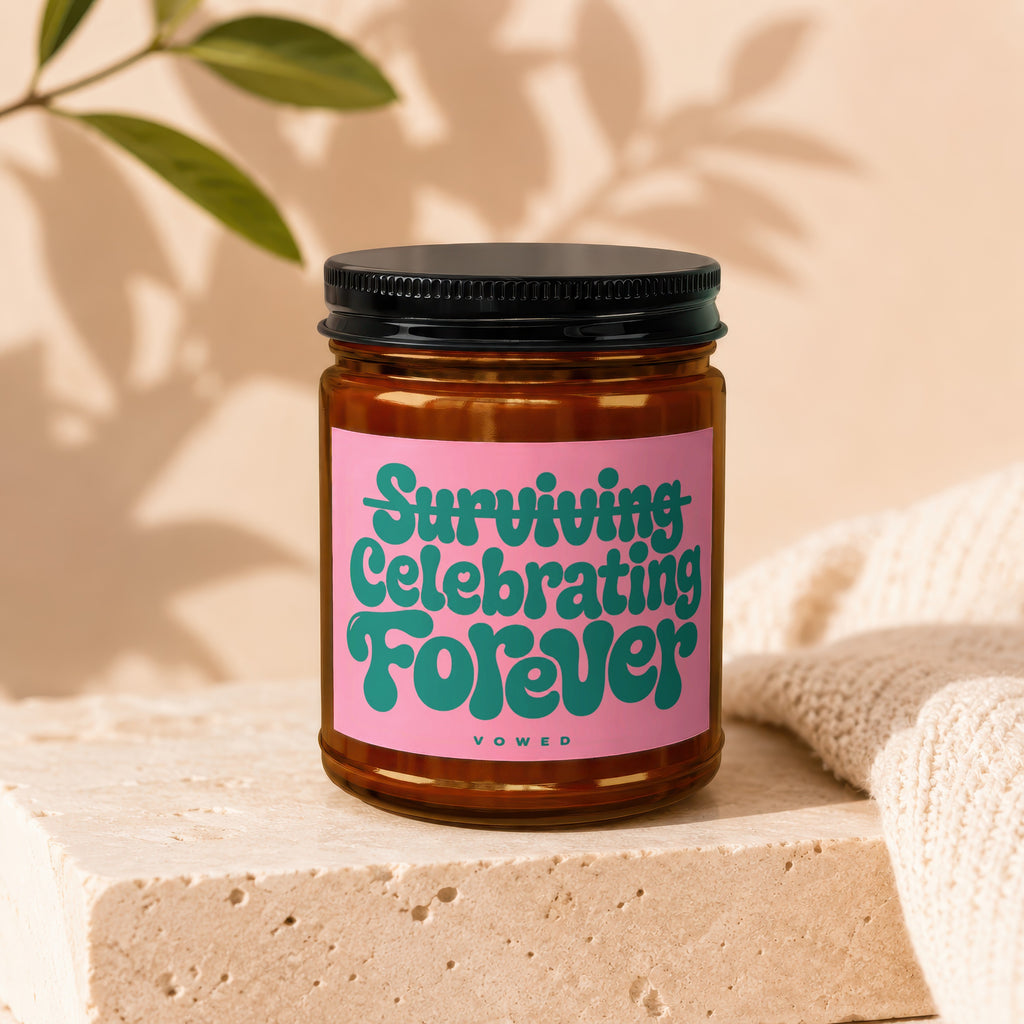Amber glass candle on stone block with pink label text "Surviving Celebrating Forever".