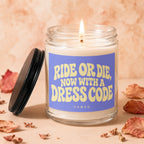 Glass candle with lid nearby, lit wick, and purple label reading "Ride Or Die, Now With A Dress Code".