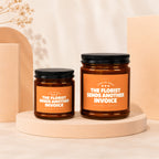 Two amber candles with black lids display orange labels stating "The Florist Sends Another Invoice."