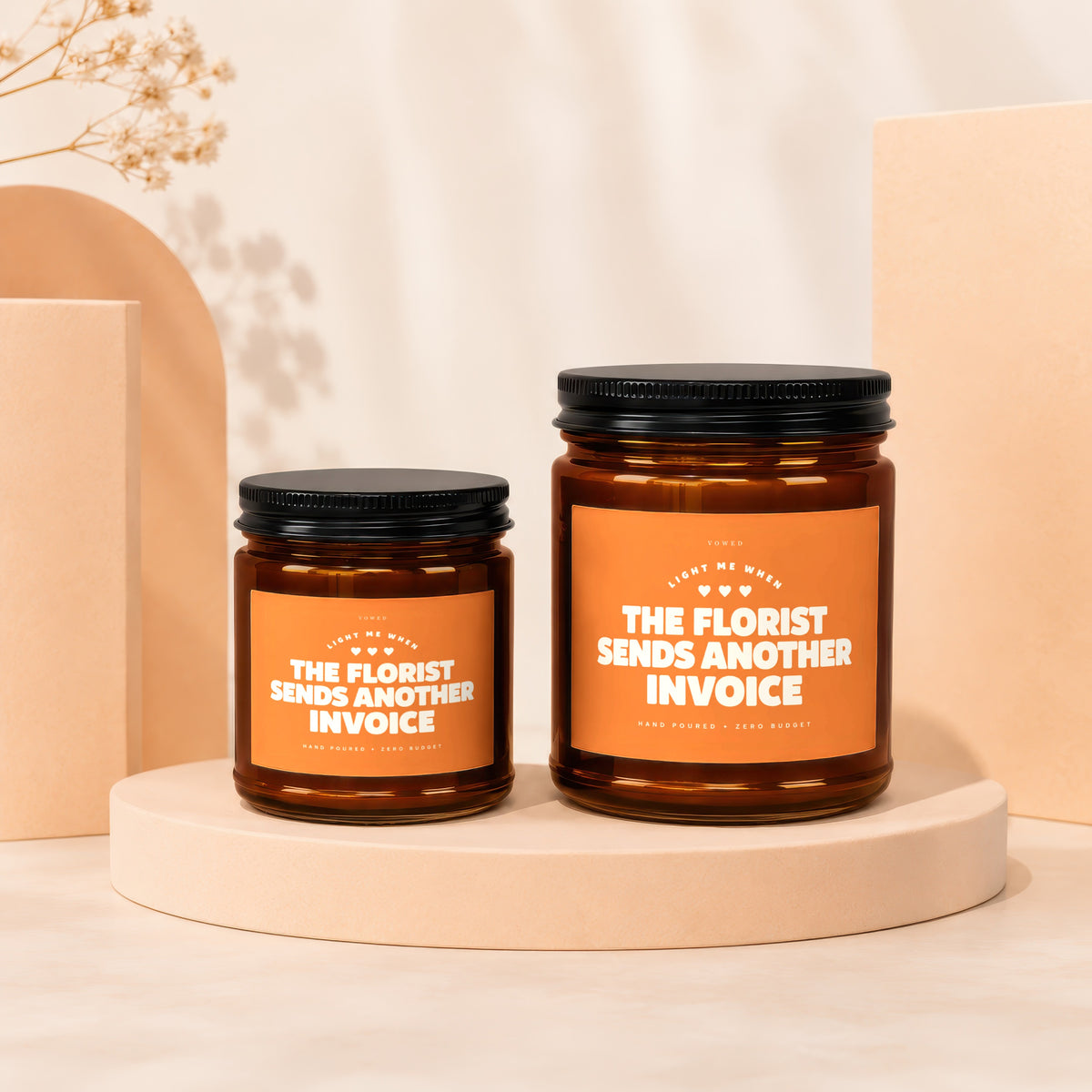 Two amber candles with black lids display orange labels stating "The Florist Sends Another Invoice."