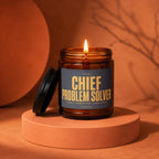 Lit candle in amber jar with label "Chief Problem Solver" on an orange pedestal.