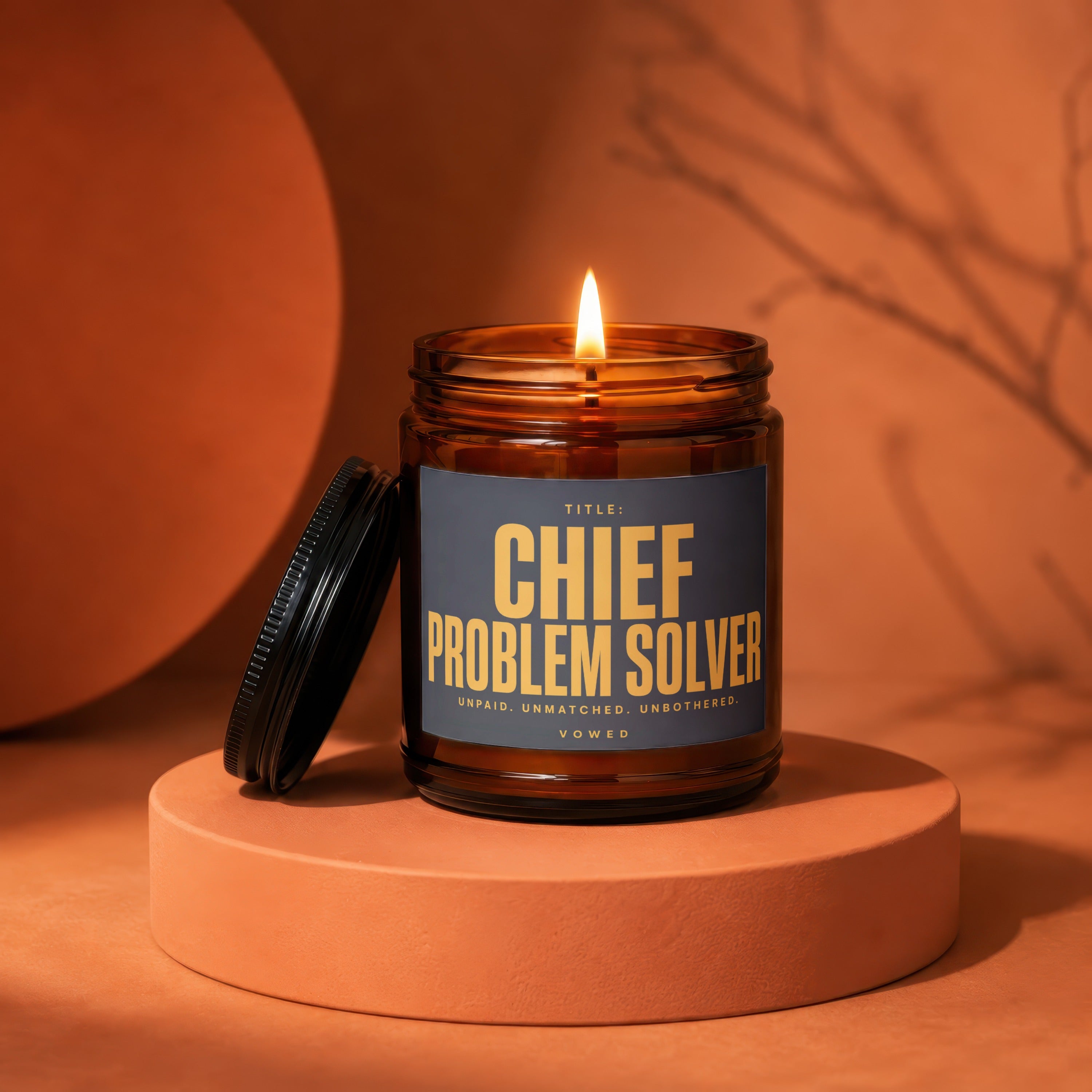 Lit candle in amber jar with label "Chief Problem Solver" on an orange pedestal.