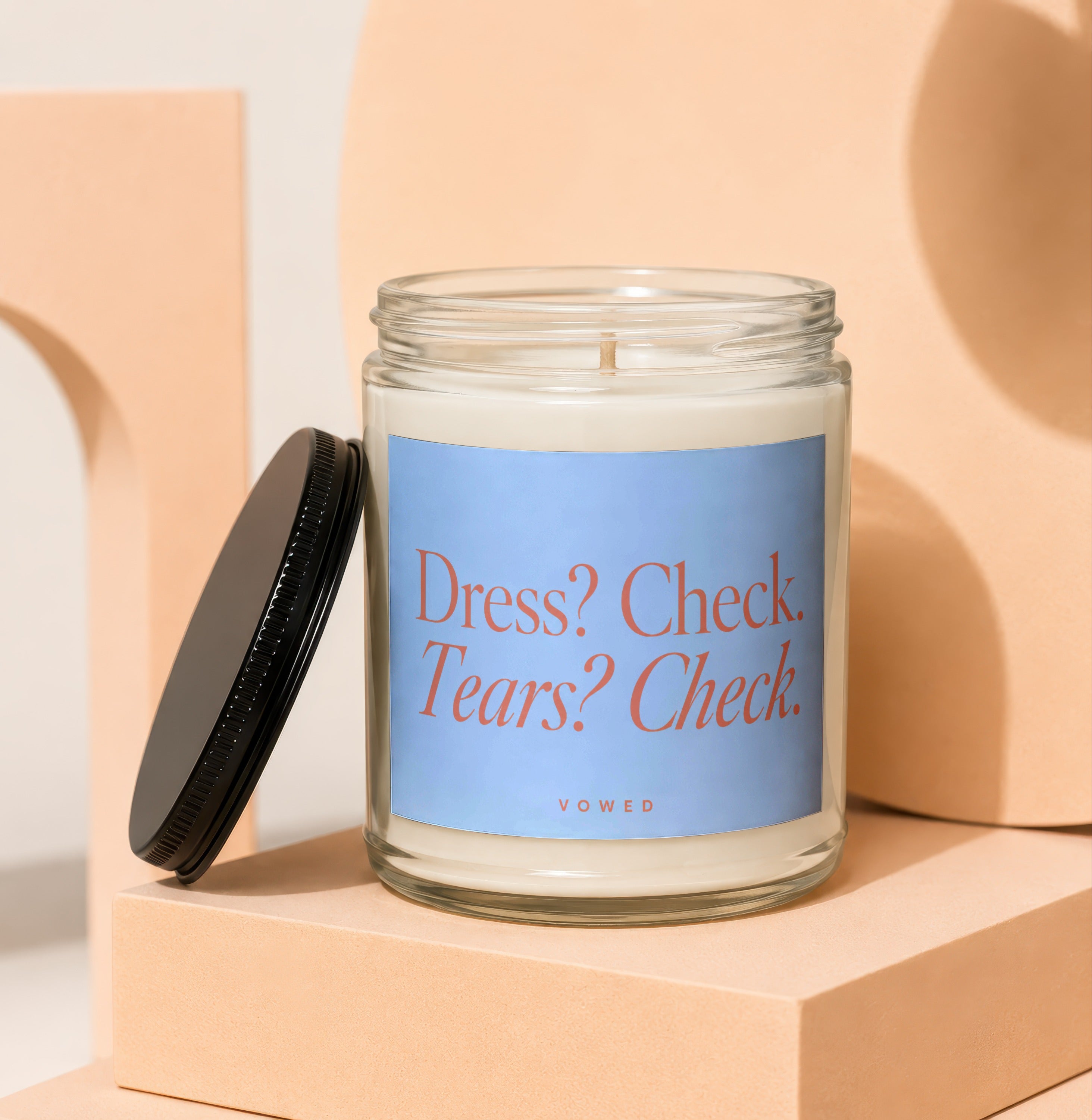 Scented candle with text "Dress? Check. Tears? Check." and "VOWED" on a blue label.