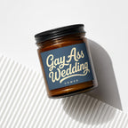 Amber glass candle with navy label reading "Gay Ass Wedding VOWED".