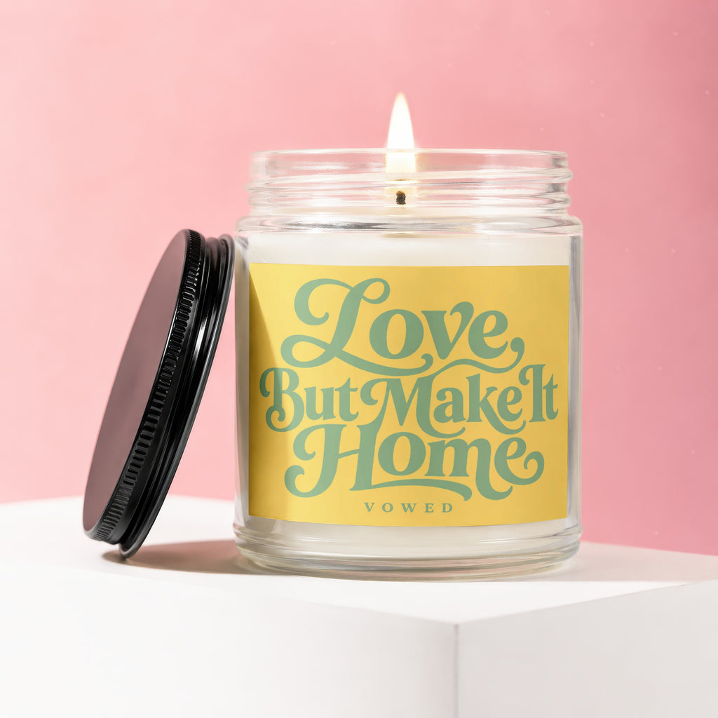 Jar candle with lit wick on a white pedestal against a pink background.