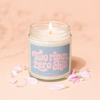 Candle with "Two rings, zero chill" text and pink petals on a peach background.