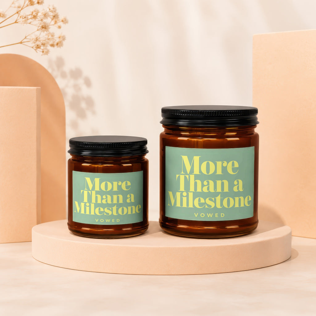 Two amber glass candles with black lids feature mint green labels reading "More Than a Milestone".