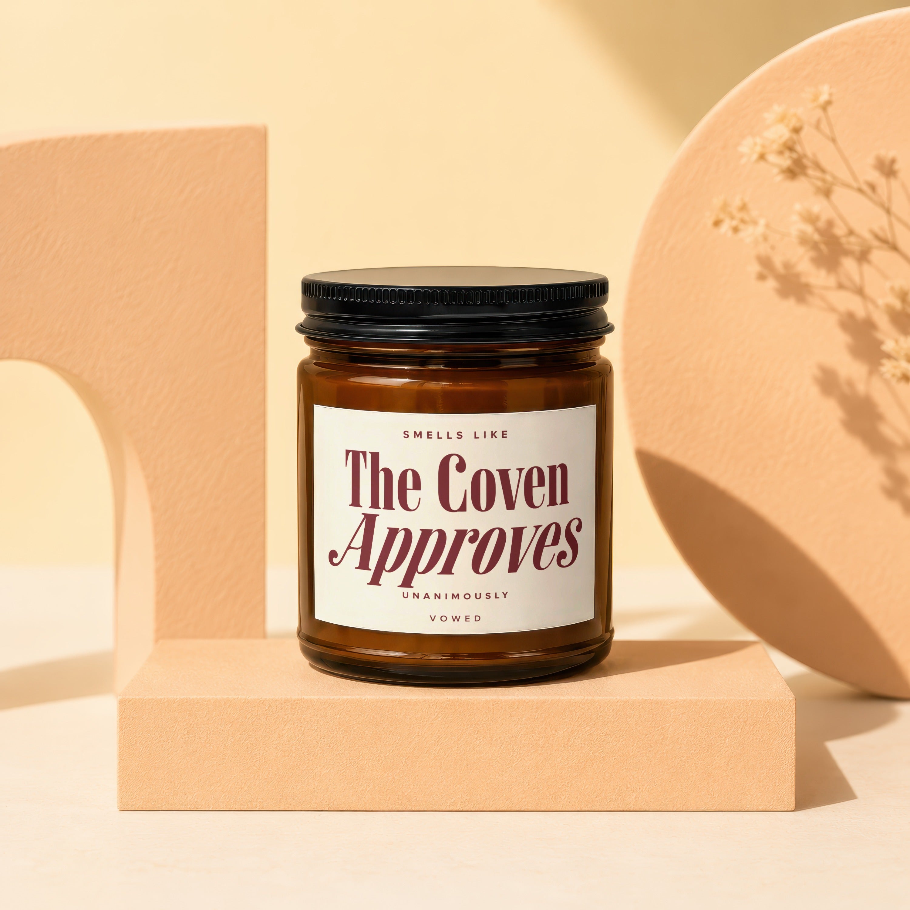 Amber jar candle with a white label reading "The Coven Approves" and "Vowed".