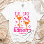 White t-shirt with "The Bach Club, Emilia's Bachelorette, Miami, FL" text and cocktail graphics.