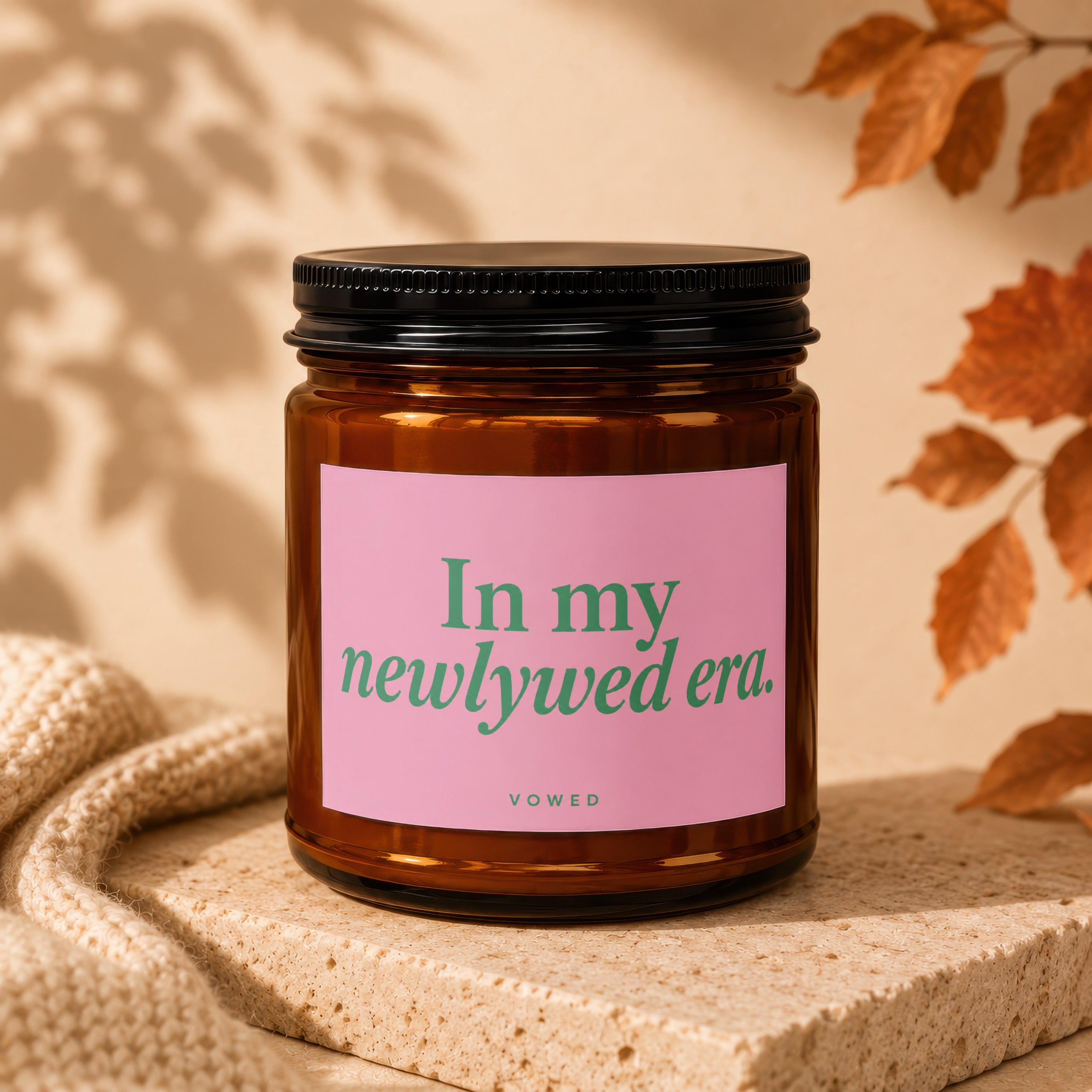 Brown glass candle with pink label reading "In my newlywed era. VOWED".