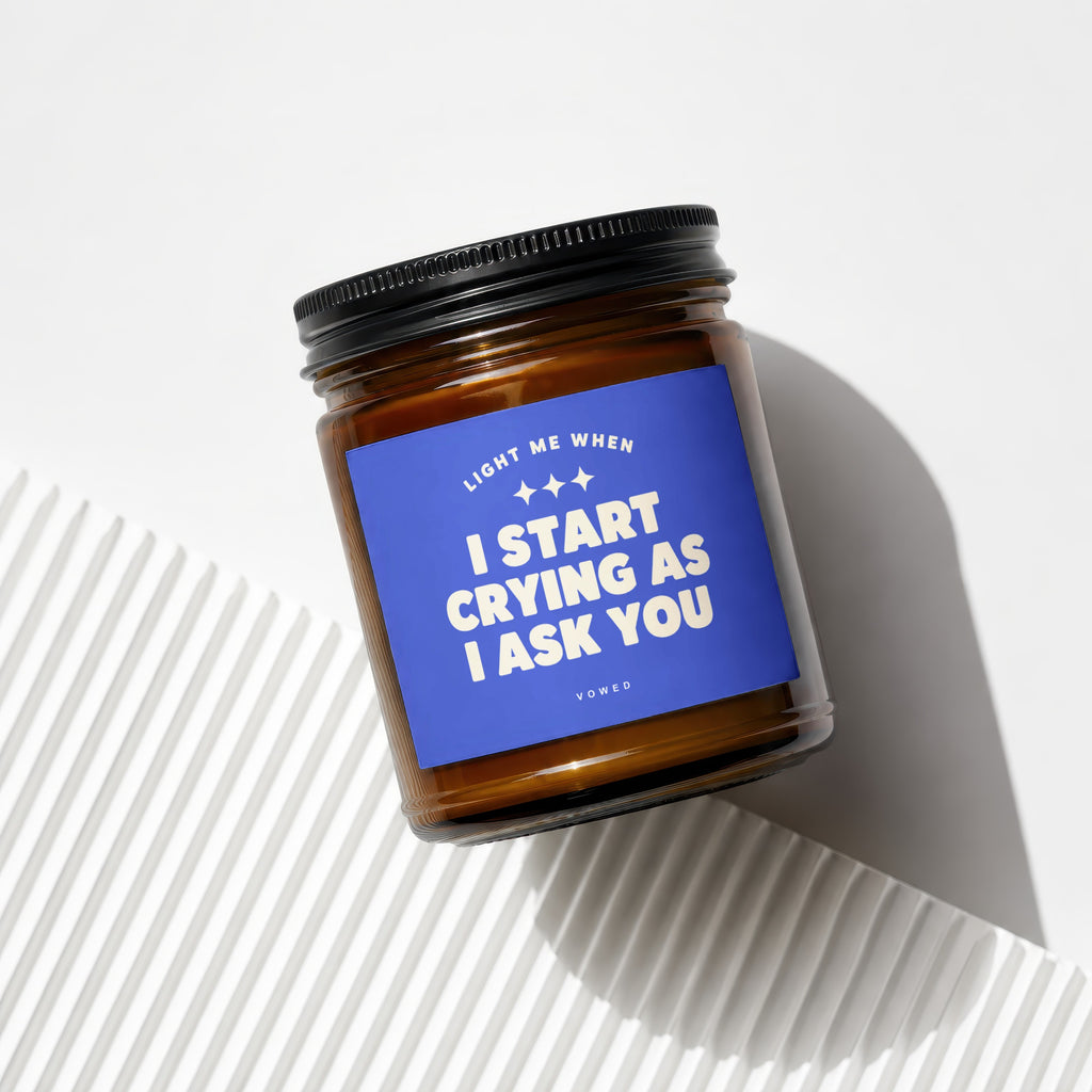 Amber glass candle with blue label reading "Light Me When I Start Crying As I Ask You".