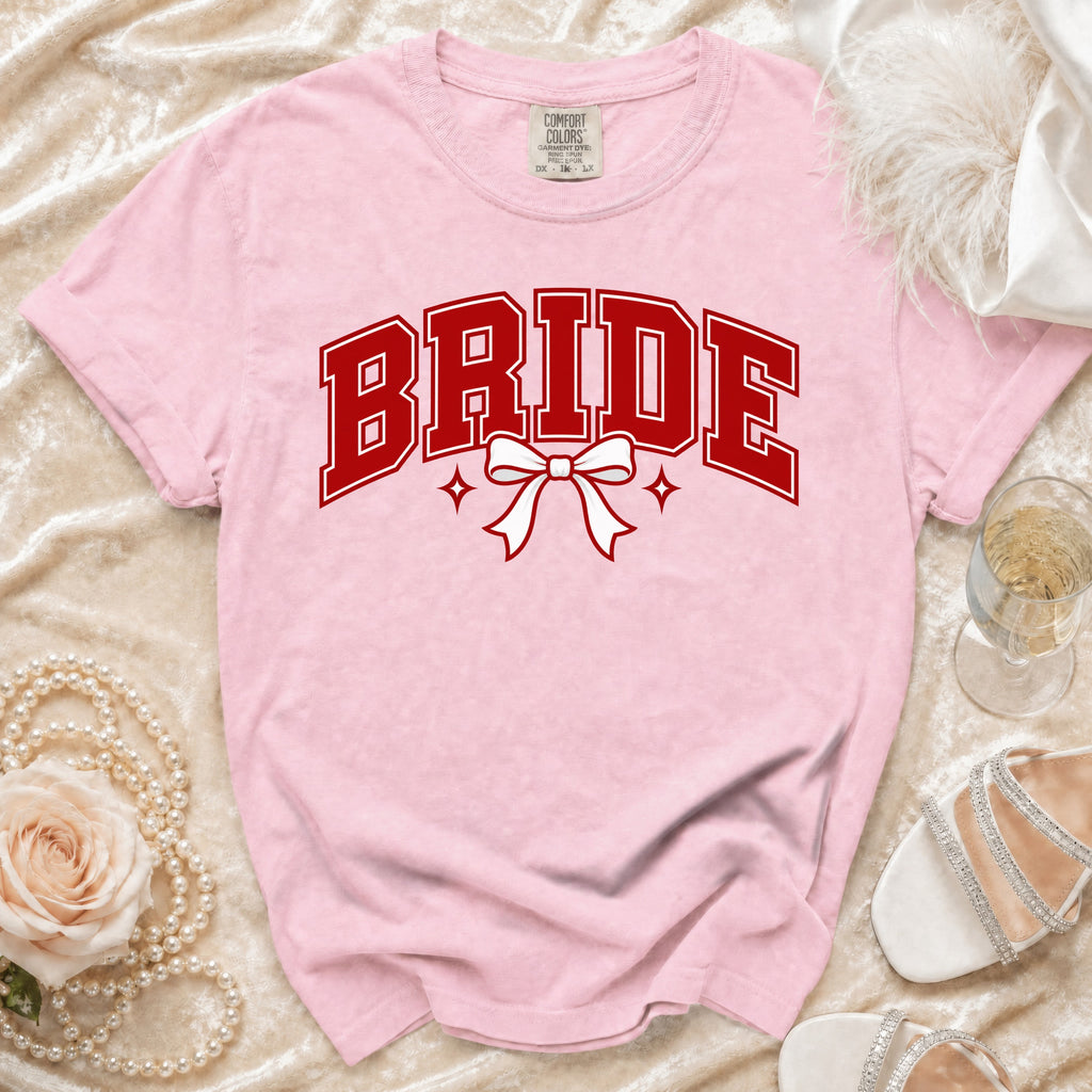 Pink t-shirt with "BRIDE" in red collegiate font and a white bow.