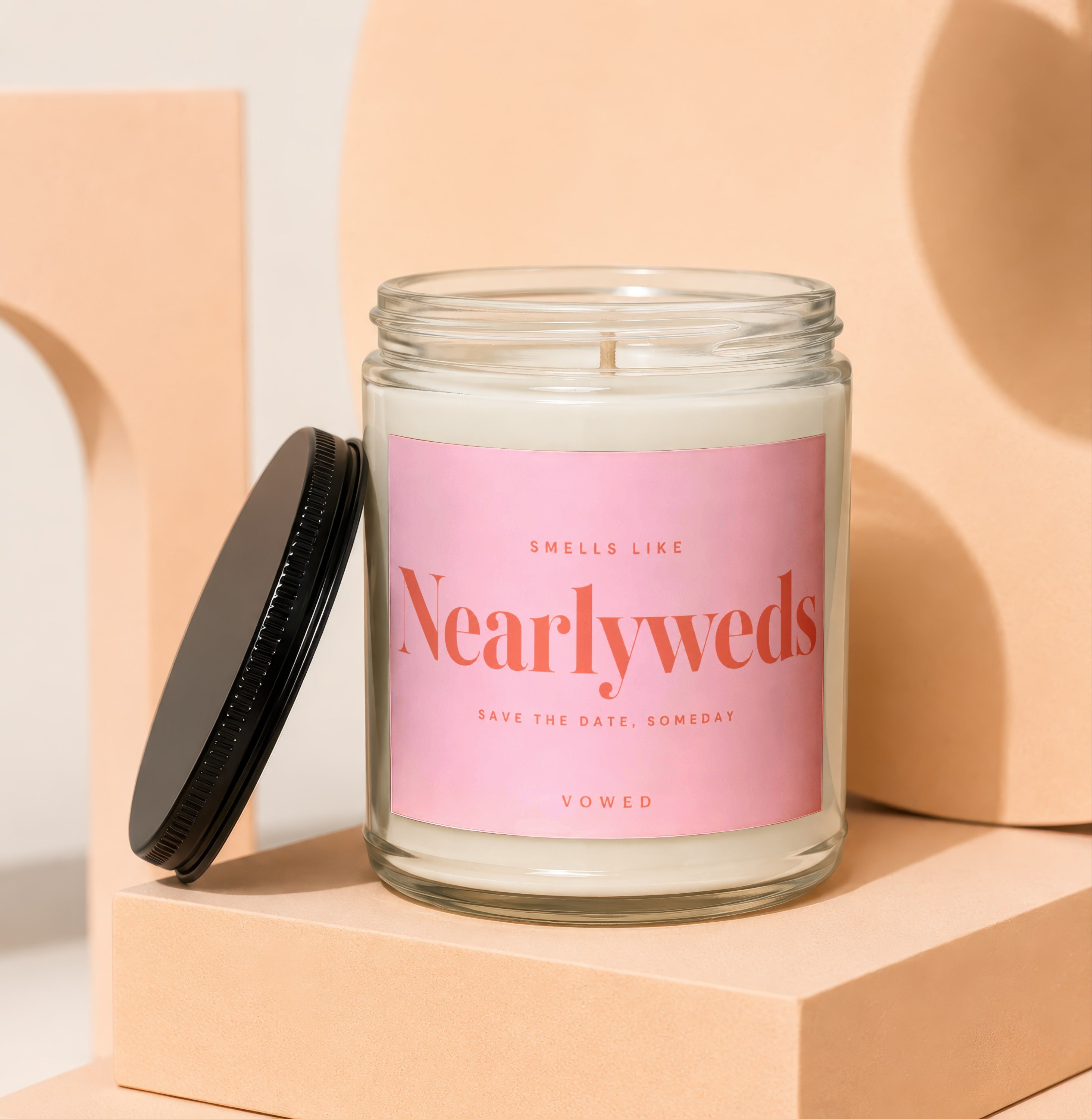 Glass candle with pink label reading "Smells Like Nearlyweds Save the Date, Someday Vowed".
