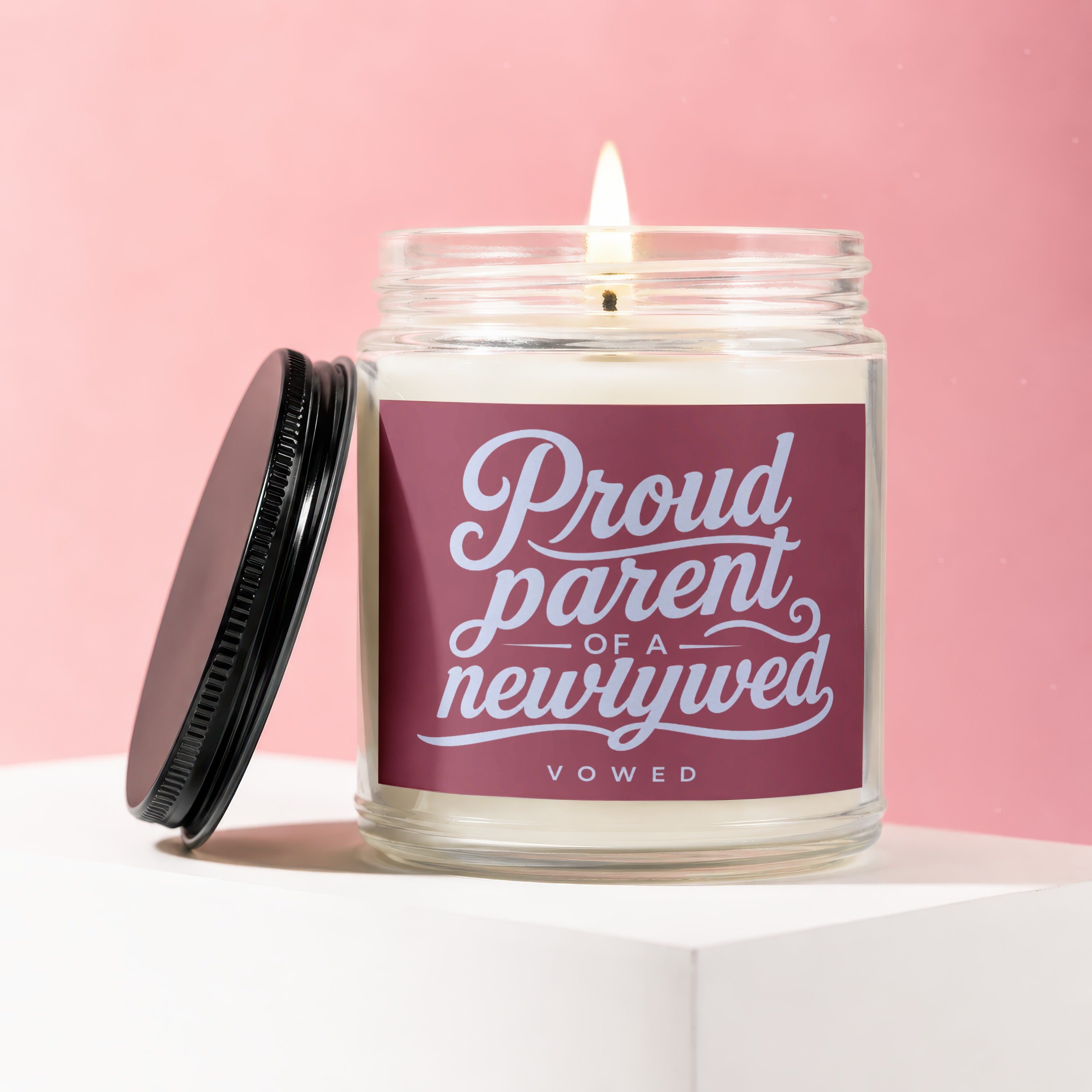 Candle with lit wick and black lid, labeled "Proud parent of a newlywed VOWED".