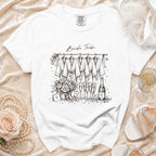 White t-shirt with "Bride Tribe" text and sketch of robes, flowers, and champagne.