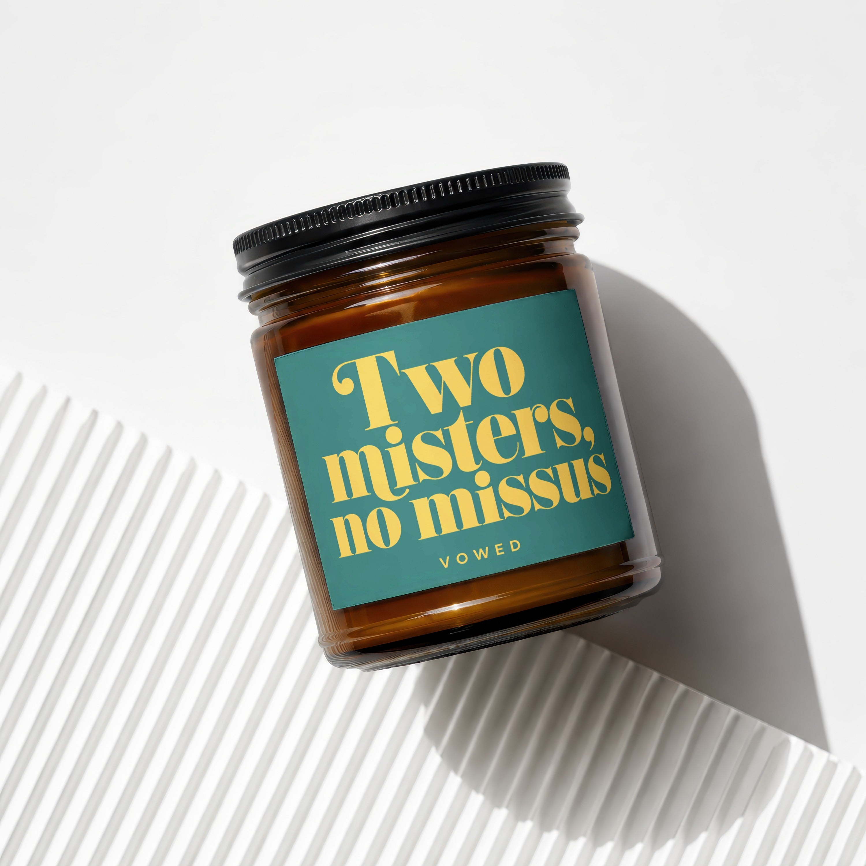 Amber glass candle with a teal label that reads "Two misters, no missus VOWED".