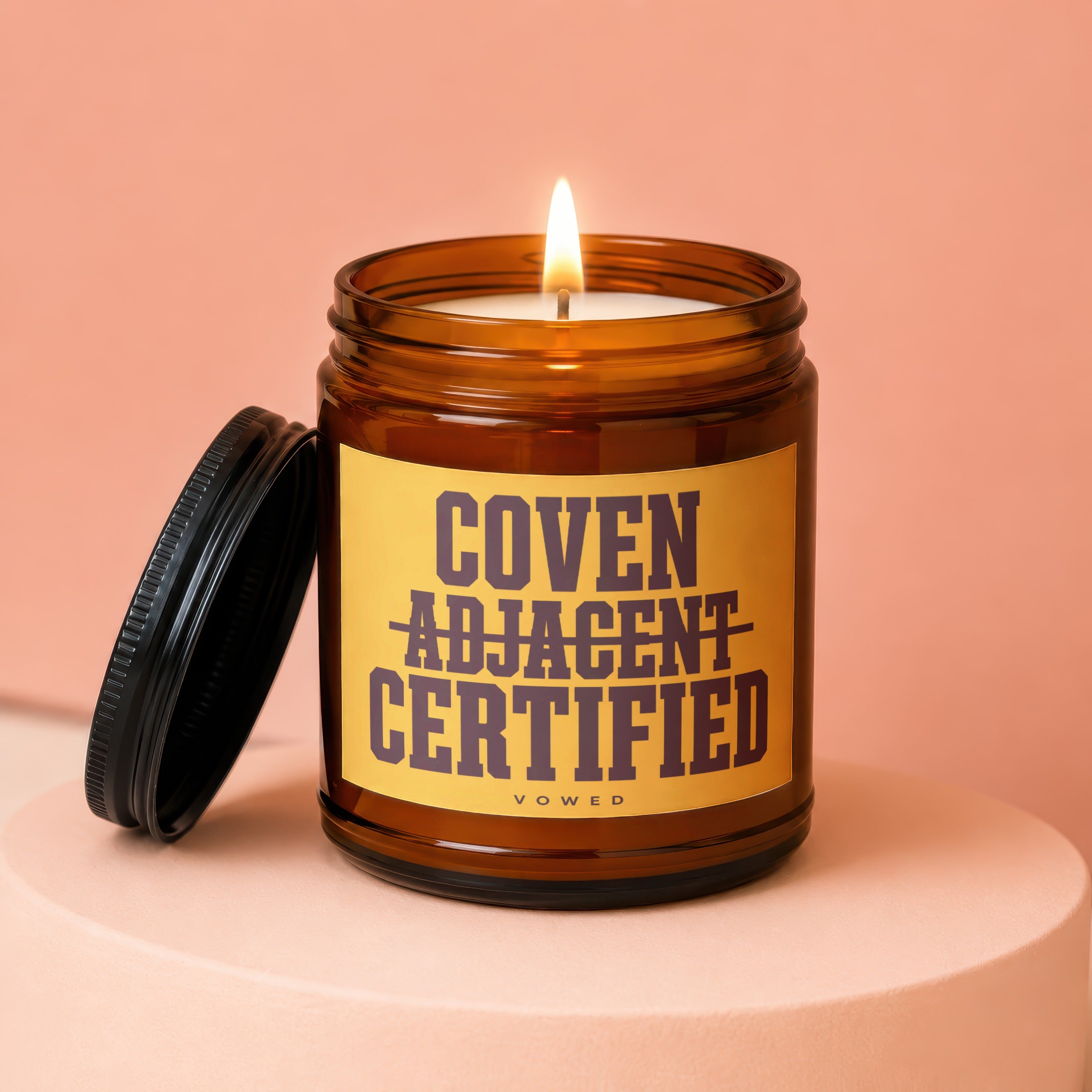 Candle in amber jar with yellow label reading "Coven Adjacent Certified"