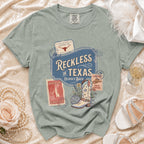 Comfort Colors t-shirt with "Reckless in Texas" and boot graphic.