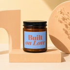 Brown glass candle with "Built on Love" on a blue label.