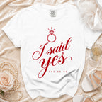 White t-shirt with red text "I said yes THE BRIDE" and diamond ring graphic.
