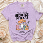 Lavender t-shirt graphic with cowgirl boots, bull skull, and guitar for "Olivia's Bach Reckless in Texas".