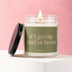 "It's giving maid of honor" candle with black lid on a pink background.