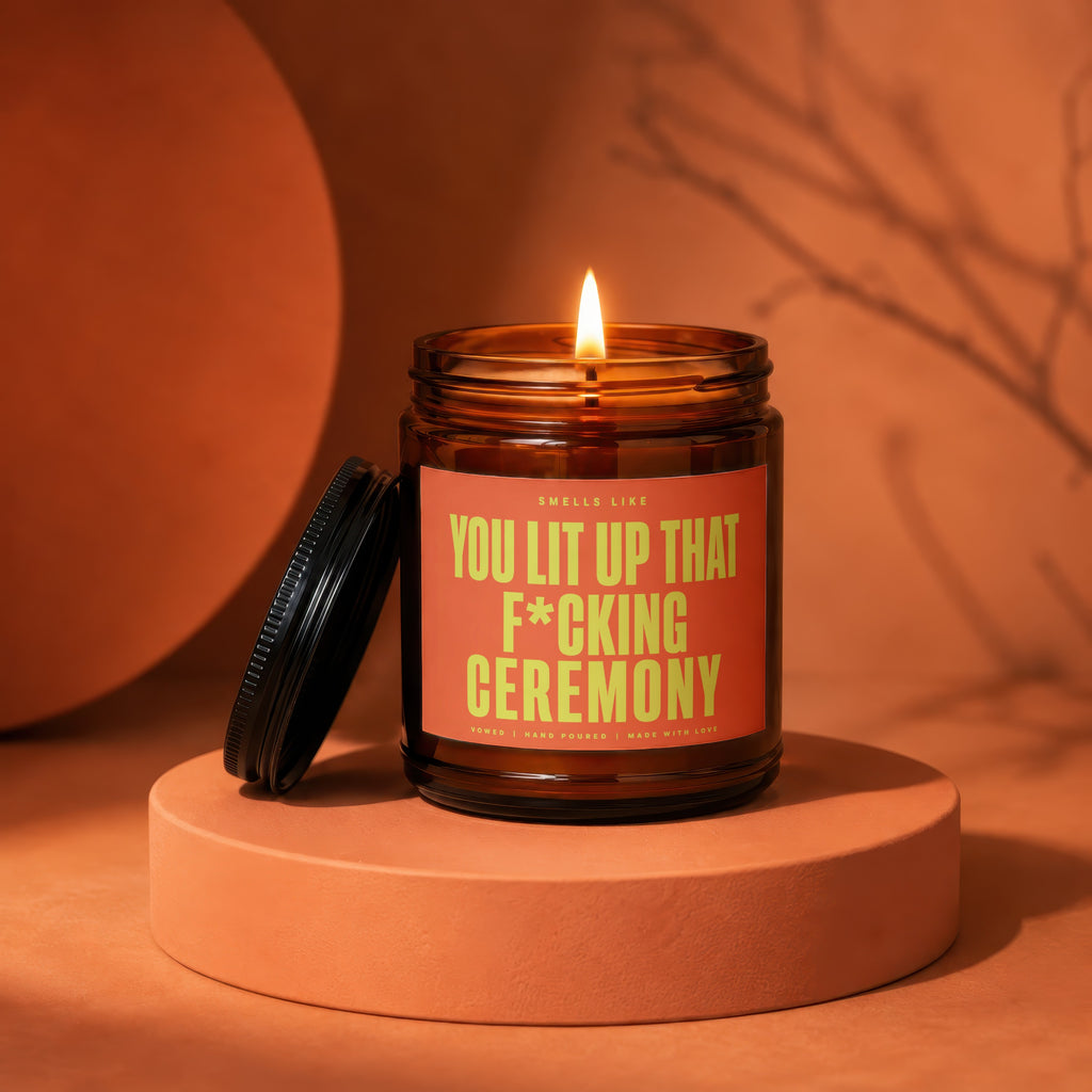 Amber jar candle with lid off, reading "You Lit Up That F*cking Ceremony".