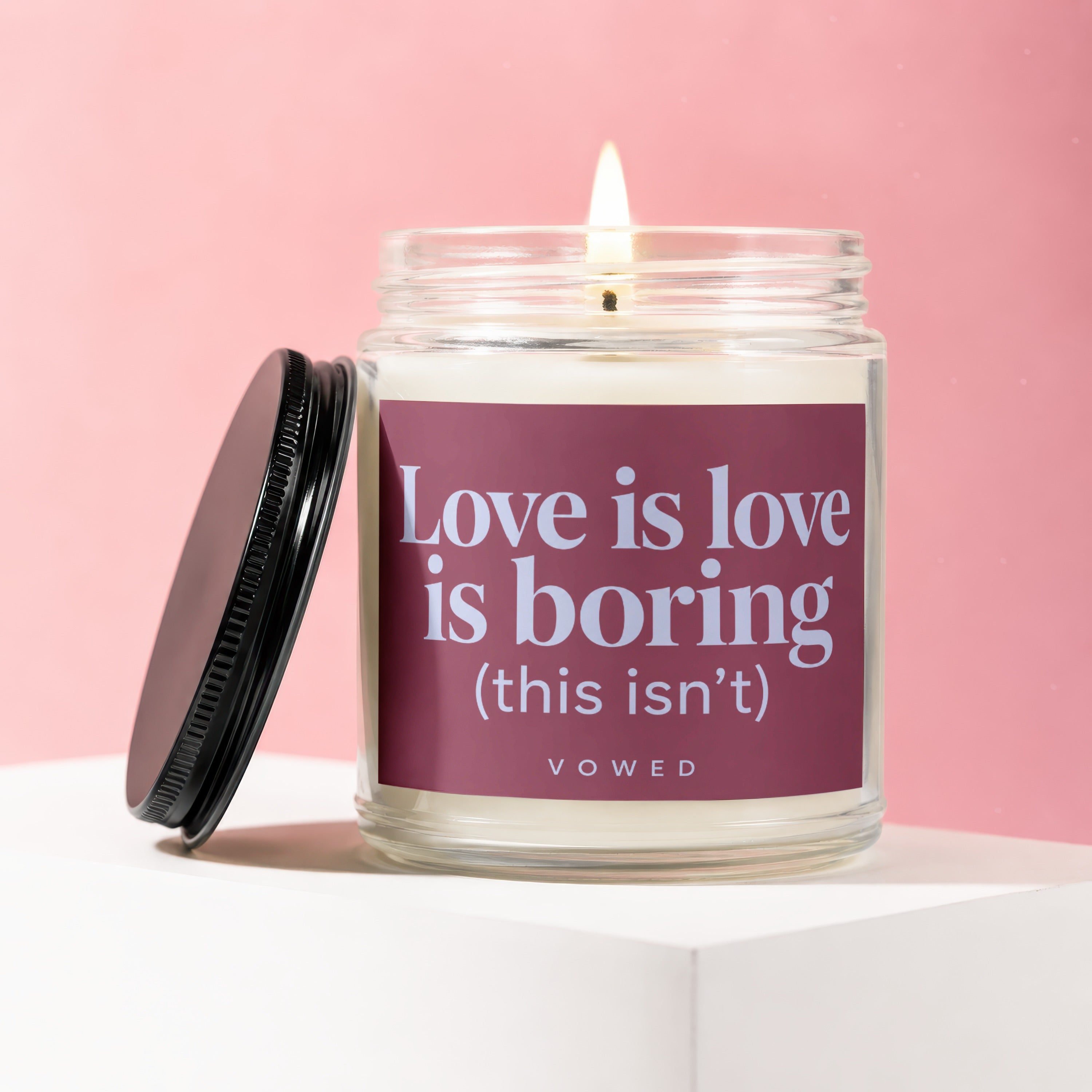 Candle with a lit wick and label reading "Love is love is boring (this isn't)".