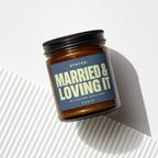 Amber glass candle with dark blue label reading "Status: Married & Loving It"